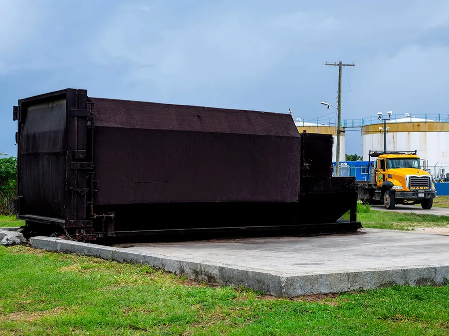 Island Sanitation Plus branded compactor bin on a concrete pad at an industrial site