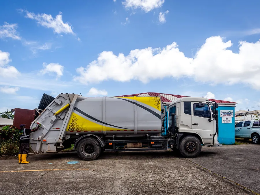 Island Sanitation Plus crew member loading a rear-loader collection truck on a commercial site